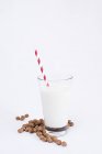 Haufen leckerer Rosinen und ein Glas frischer Milch mit gestreiftem Stroh auf weißem Hintergrund — Stockfoto