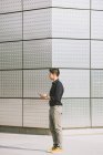 Homem elegante usando telefone celular enquanto está de pé contra a parede do edifício — Fotografia de Stock