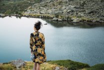 Woman on rocks of small lake in mountains, rear view — Stock Photo