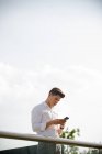 Fiducioso giovane uomo d'affari utilizzando smartphone in piedi alla ringhiera — Foto stock