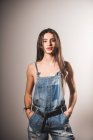 Сексуальная девушка в джинсовом комбинезоне над обнаженным телом позирует на сером фоне — стоковое фото