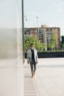Homme élégant confiant dans des lunettes de soleil marchant en ville — Photo de stock