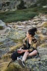 Jeune femme brune assise avec du café sur des pierres dans la vallée — Photo de stock