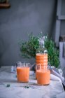 Бутылки и стаканы с вкусным здоровым напитком, стоящим на мраморном столе в стильном номере — стоковое фото