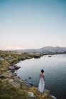 Giovane donna in piedi da sola sulla riva del lago di montagna — Foto stock