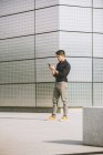 Uomo elegante utilizzando il telefono cellulare mentre in piedi contro muro edificio — Foto stock