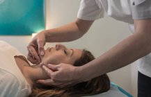 Terapeuta massaggiando viso femminile in sala massaggi — Foto stock