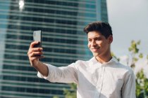 Молодий бізнесмен бере селфі зі смартфоном проти сучасної будівлі — стокове фото