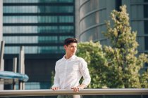 Lächelnder junger Geschäftsmann steht am Geländer eines modernen Wolkenkratzers — Stockfoto