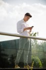 Fiducioso giovane uomo d'affari utilizzando smartphone in piedi alla ringhiera — Foto stock