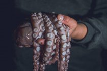 L'homme tient une pieuvre crue dans ses mains. Photo sombre. — Photo de stock