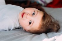 Bambino divertente sdraiato sul letto e guardando la fotocamera — Foto stock
