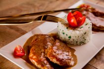 Carne asada con salsa y arroz en bandeja blanca con tenedor y cuchillo - foto de stock