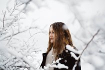 Hübsche Frau steht in weißen Raureif-Zweigen und blickt in die Kamera. — Stockfoto
