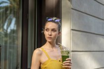 Smiling woman in summer dress standing with drink and looking away — Stock Photo