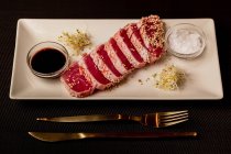 Raw sliced tuna steak on platter with sauce on black background — Stock Photo