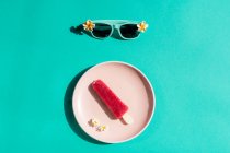 View from above of pink ice cream on white plate and sunglasses on blue background — Stock Photo