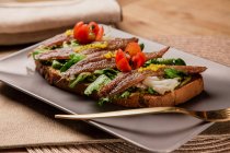 Сэндвич с овощами и рыбой на серой тарелке с вилкой — стоковое фото