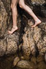 Crop unrecognizable barefoot woman stepping on rough rocks. — Stock Photo