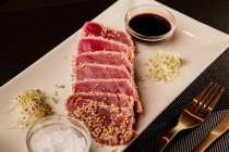 Steak de thon tranché cru sur plateau avec sauce sur fond noir — Photo de stock
