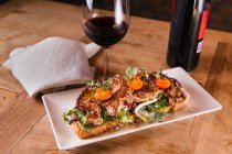 Panino con carne e verdure fritte e bicchiere di vino rosso sul tavolo di legno — Foto stock