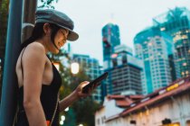 Seitenansicht einer Asiatin in stylischer Kleidung, die auf der Straße steht und ihr Smartphone benutzt. — Stockfoto