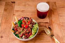 Чаша вкусного овощного салата с авокадо на деревянном столе со стаканом пива — стоковое фото