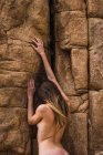 Back view of naked woman climbing up on rough mountain wall. — Stock Photo