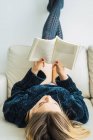 Chica rubia absorbida con la lectura en el entrenador en casa - foto de stock