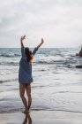 Женщина с длинными каштановыми волосами стоит на пляже с поднятыми руками — стоковое фото