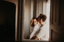 Romantic couple embracing at window at home — Stock Photo