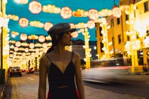Alla moda giovane donna asiatica guardando lontano in città illuminata la sera. — Foto stock