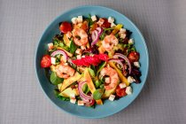 Vegetable salad with shrimps in blue bowl on grey surface — Stock Photo