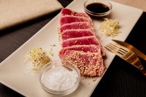 Bife de atum fatiado cru na bandeja com molho no fundo preto — Fotografia de Stock