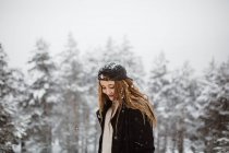 Seitenansicht einer hübschen Frau, die bei Schneefall auf der Straße steht und in die Kamera schaut. — Stockfoto