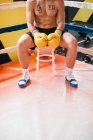Boxer sicuro di sé senza maglietta in guanti seduto su sgabello sul ring. — Foto stock