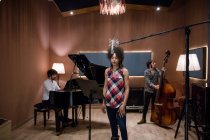 Lovely woman in casual outfit singing nice song white rehearsing with band in recording studio. — Stock Photo