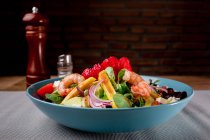 Vegetable salad with shrimps in blue bowl on grey surface — Stock Photo