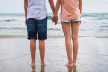 Amici adolescenti in piedi e si tengono per mano sulla spiaggia — Foto stock