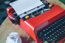 Красная пишущая машинка крупным планом на маленьком столе с вставленным листом бумаги — стоковое фото