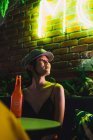 Stilvolle junge Asiatin sitzt im Café und trinkt eine Flasche — Stockfoto