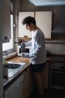 Hombre en pijama vertiendo café en taza en la cocina - foto de stock