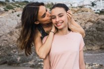 Donna abbracciare e baciare figlia sorridente in riva al mare sfondo in estate — Foto stock