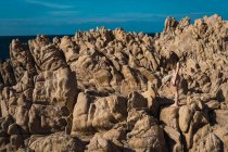 Vista lateral de mujer desnuda atractiva irreconocible de pie sobre roca en día soleado. - foto de stock