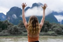 Back view of woman standing with hands up on background of green mountains. — Stock Photo
