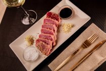 Steak de thon tranché cru sur plateau avec sauce sur fond noir avec verre de vin blanc — Photo de stock