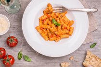 Top view of appetizing pasta with tomatoes on plate with fork. — Stock Photo