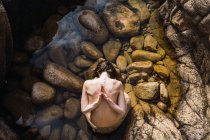 Dall'alto donna nuda seduta con le mani dietro la schiena su pietre. — Foto stock