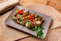 Сендвіч з овочами та рибою на сірій тарілці на килимку — стокове фото