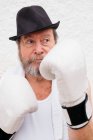 Erwachsener Mann mit Hut und weißen Boxhandschuhen an rauer Wand. — Stockfoto